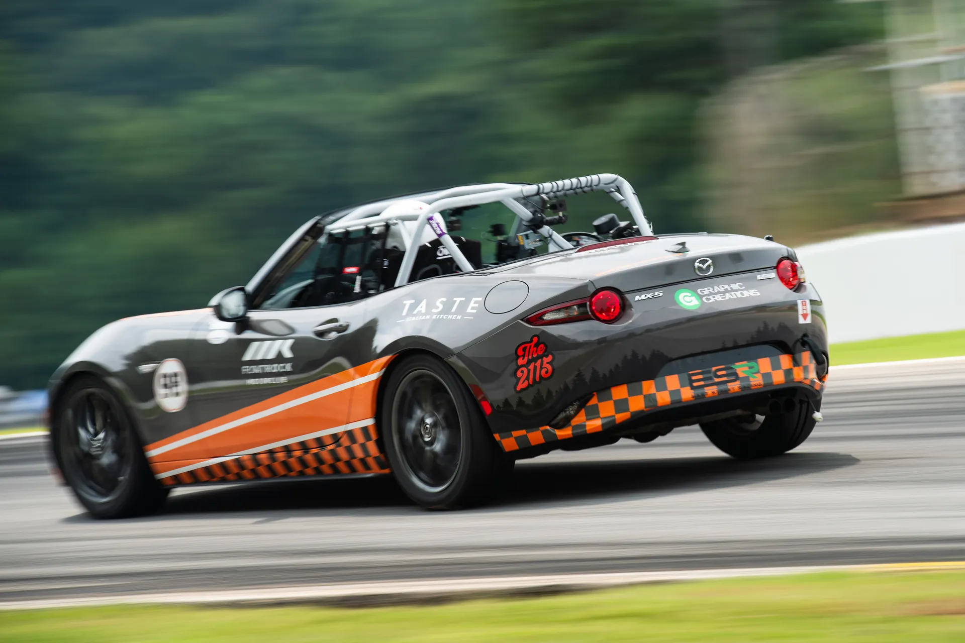 The University of Tennessee’s No. 98 Rocky Top Racing Mazda MX-5, gray with orange checkerboard and sponsor logos, at speed at Michelin Raceway Road Atlanta.